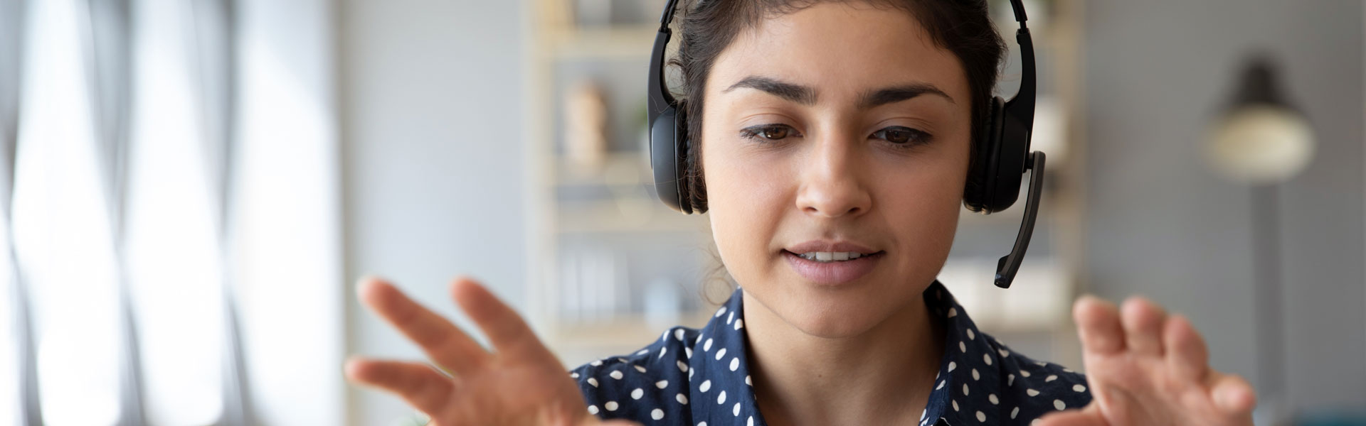 Young woman with headphones and her hands raised during videoconference on laptop